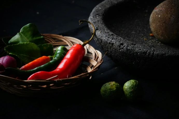 Chili peppers, lime, and herbs in a basket with mortar