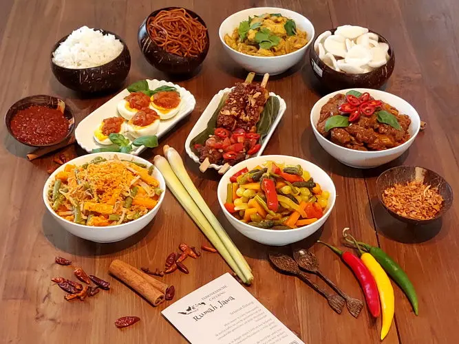 Rijsttafel Kartini (Daging saos tiram – rundvlees in oestersaus, Ayam bumbu rujak – kip in pikante saus, Cap cai – gebakken groenten in knoflook, Gado-Gado - Javaanse salade met pindasaus, Sate ayam – kip saté met pinda saus, Opor telur – gekookt ei in gele kokossaus, Bami Goreng - gebakken noedels, Verpakking in Rumah Jawa-stijl)